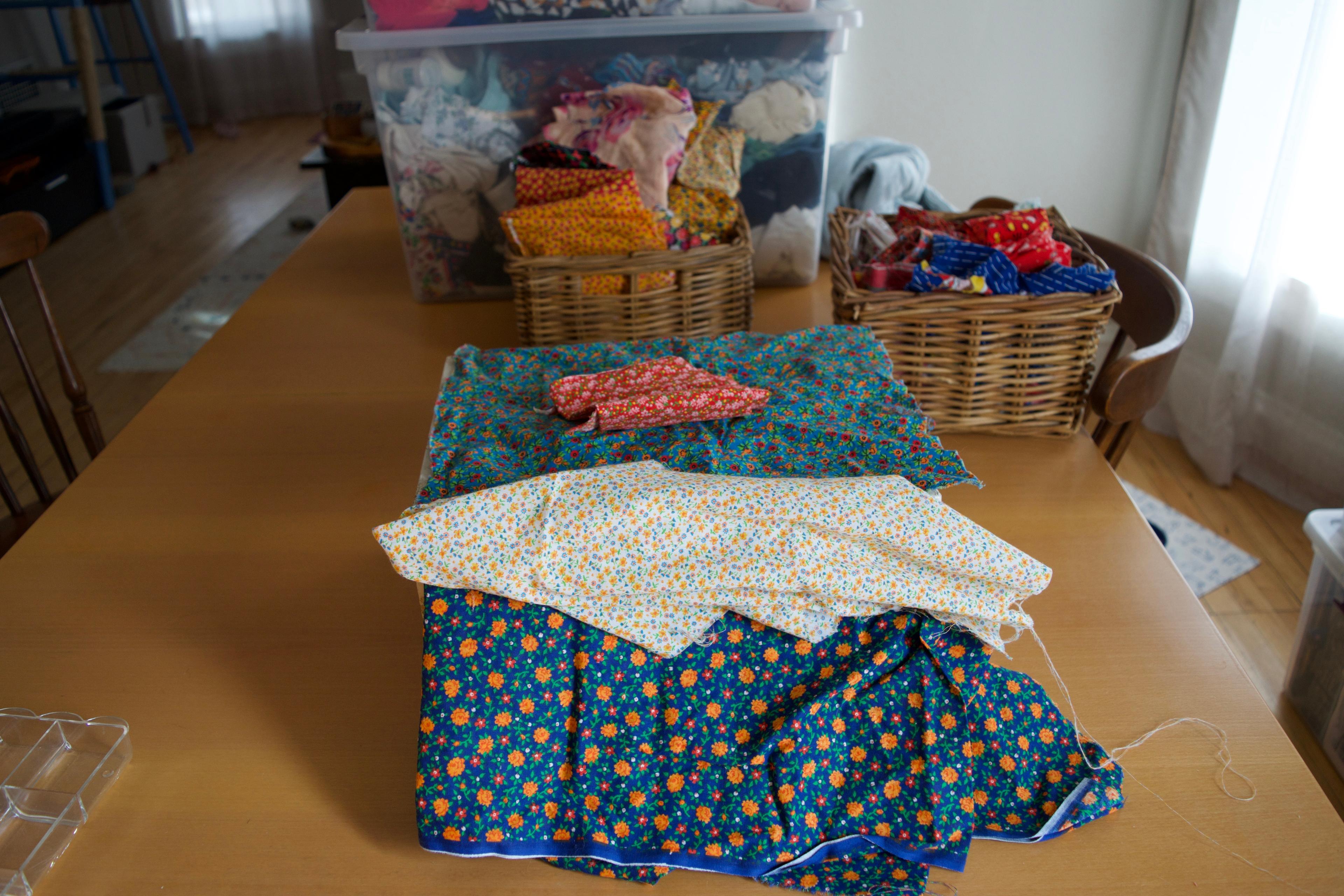 A selction of blue, white and red fabrics laying on the sewing box. There are bins of fabric on the table in the background.