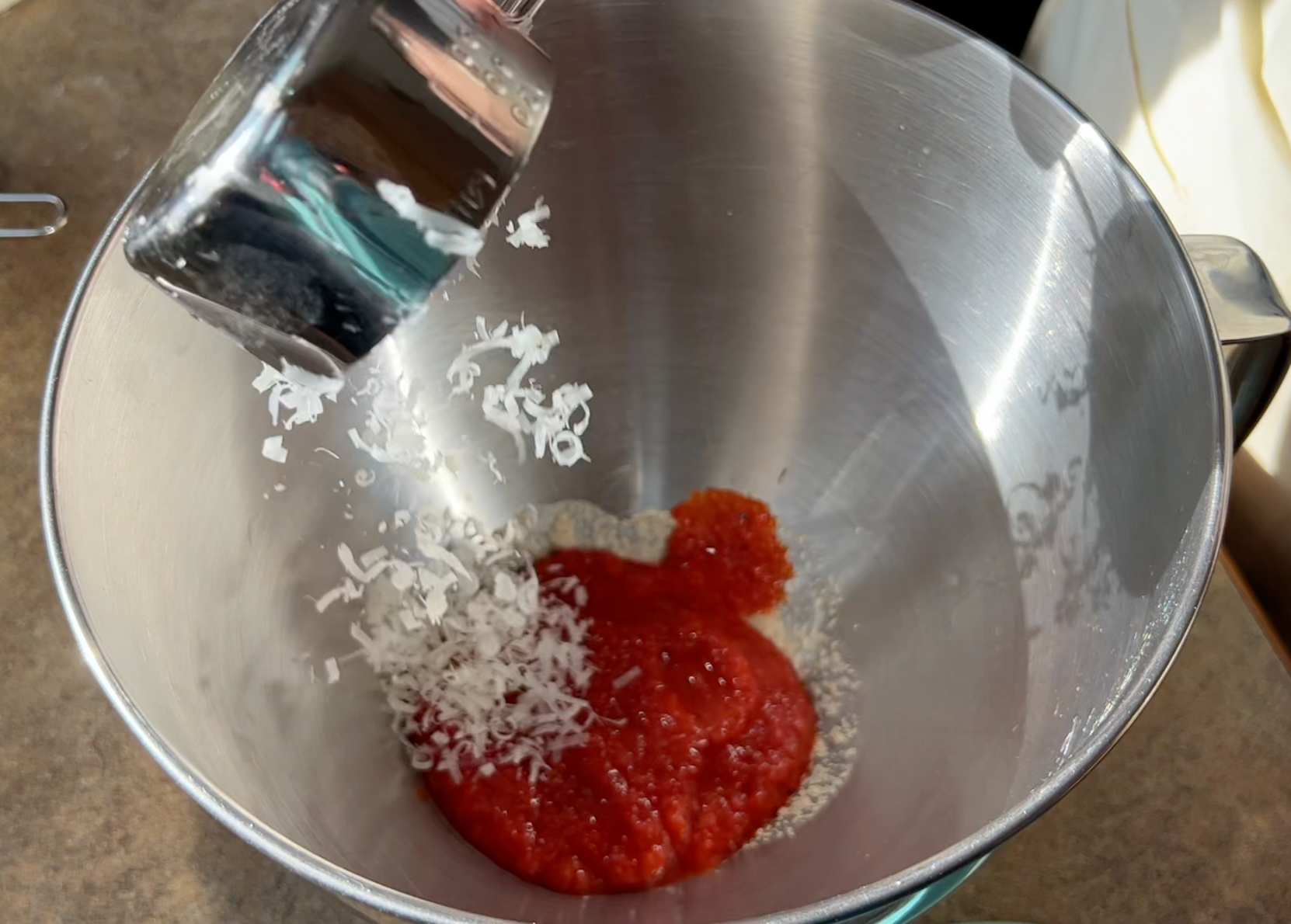 Pouring grated cheese into a stainless steel bowl with pureed red pepper