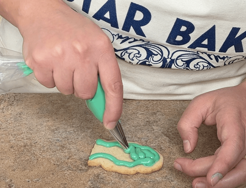 Piping green icing onto a cookie
