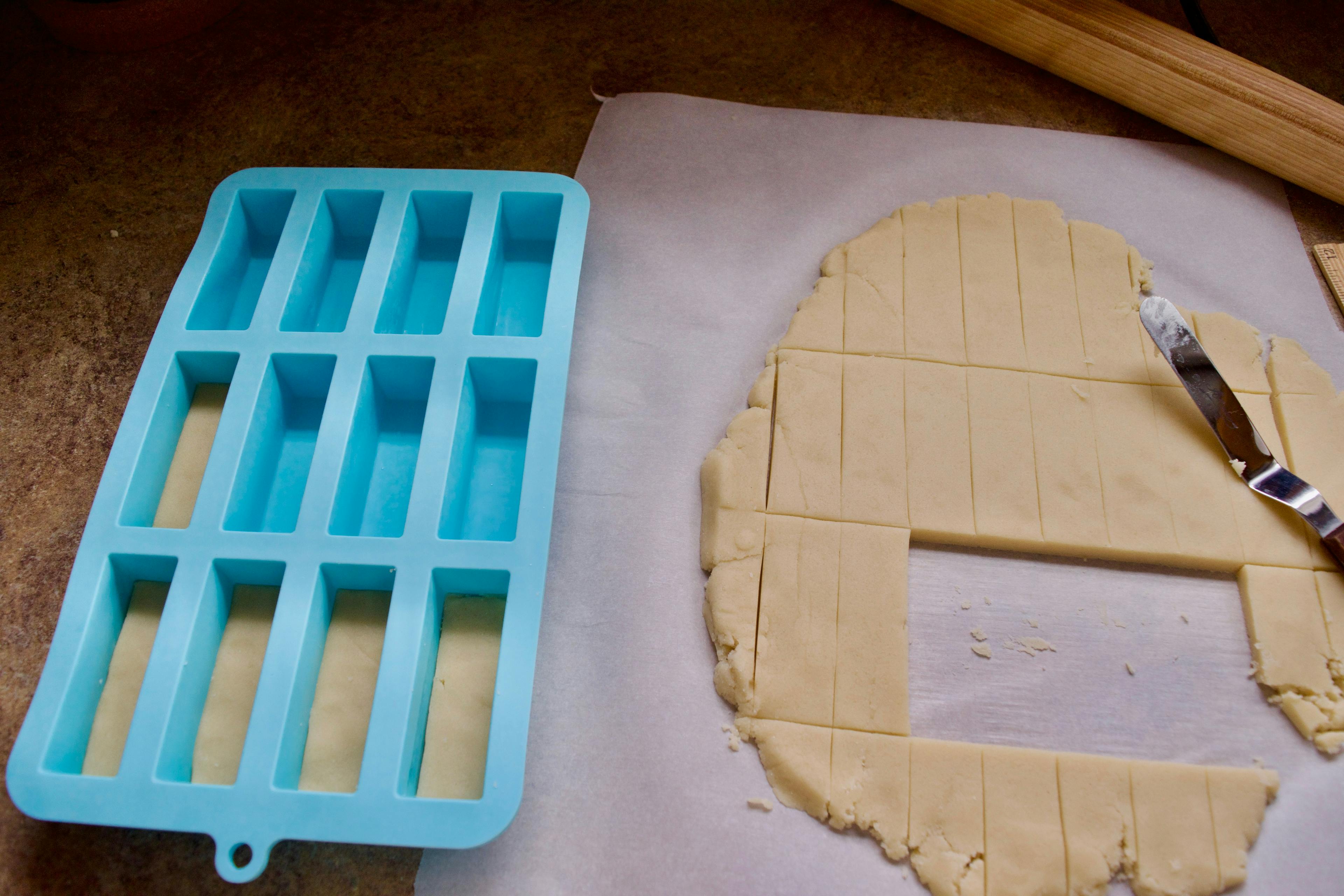 Placing the cut rectangles of dough into a blue silicone mold of 12 small rectangles.