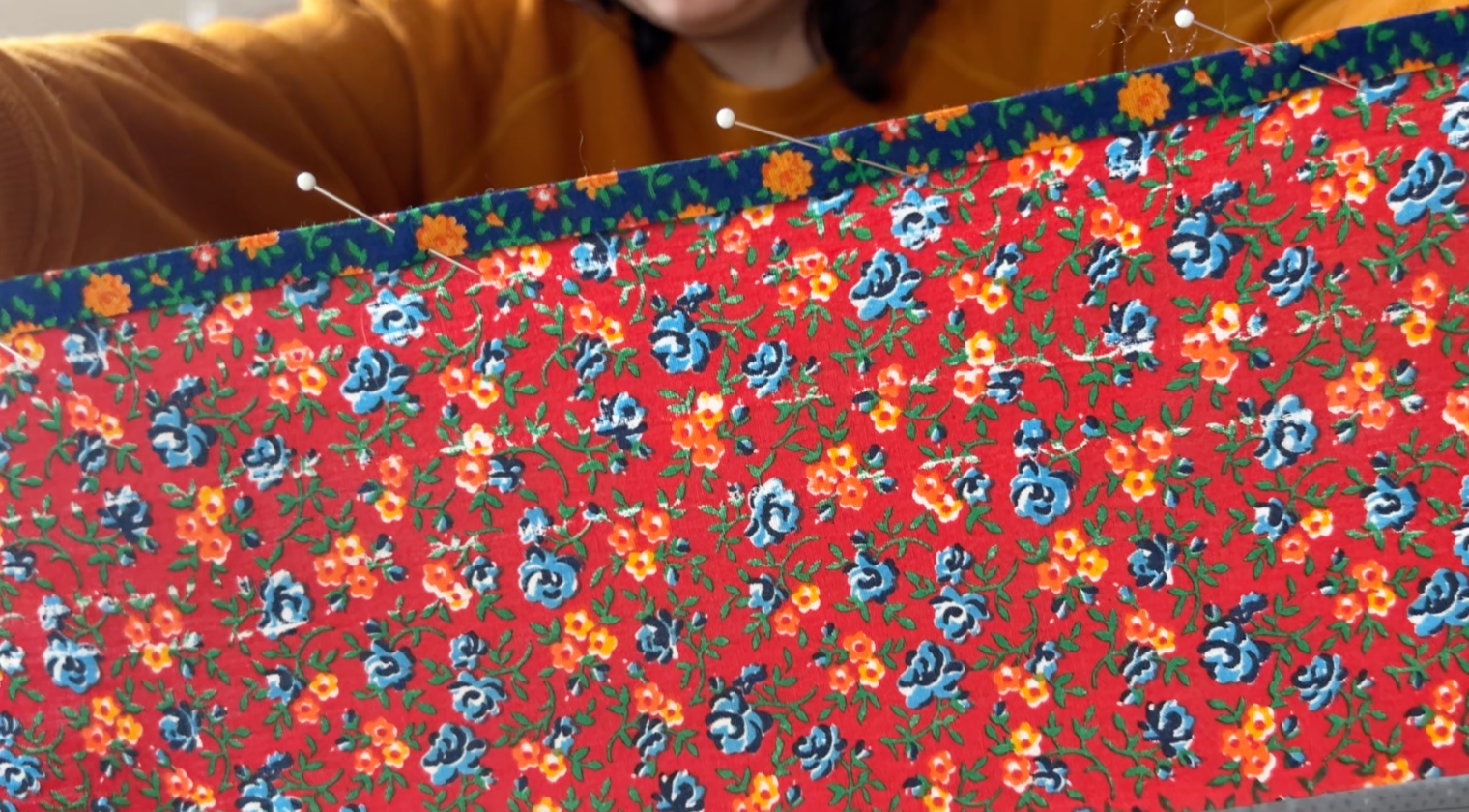 A blue strip made with the bias tape maker pinned to the top of a piece of red floral fabric