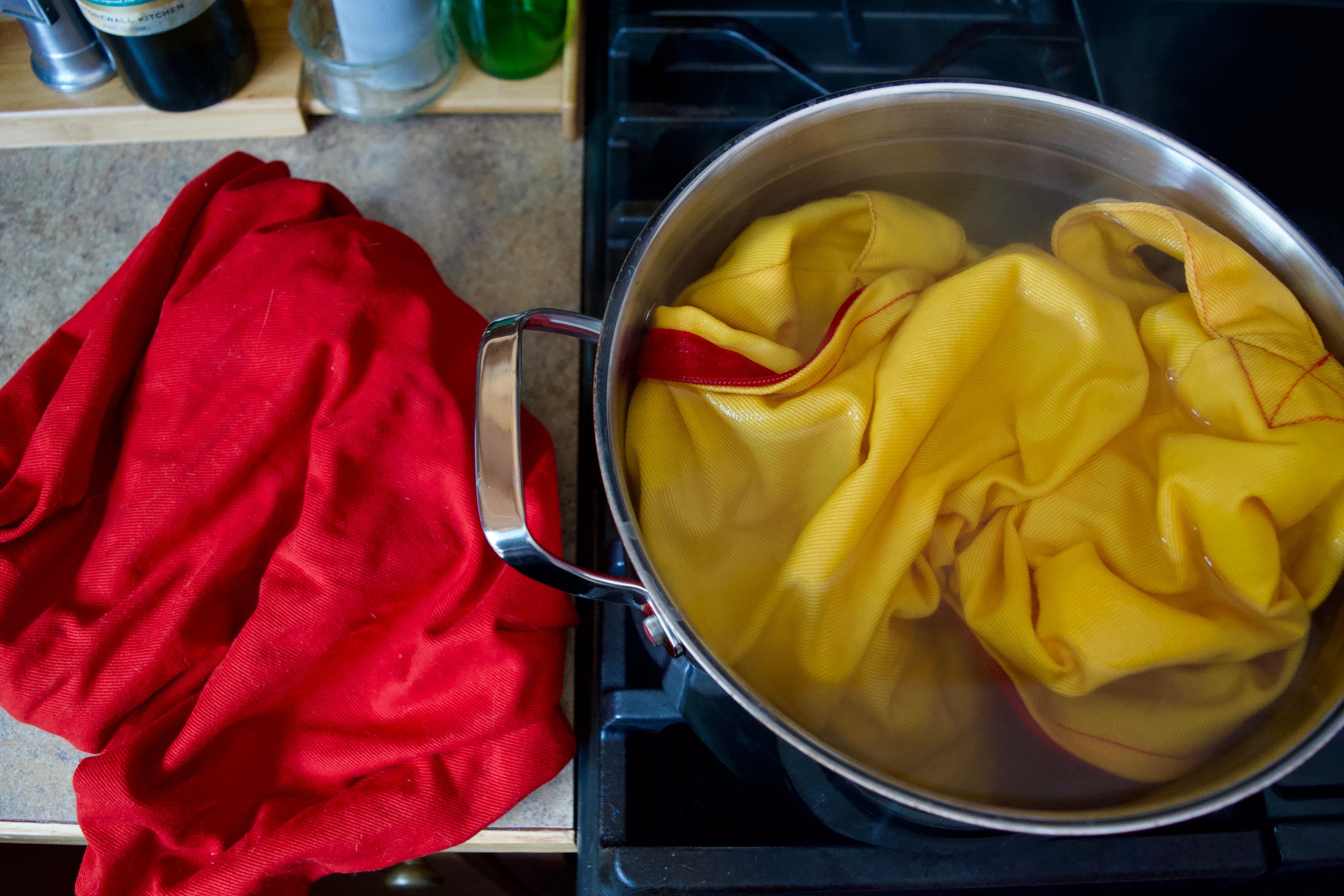 One yellow yoga bolster cover in a pot of murky water on the stove and one red yoga bolster cover on the counter next to the stove.