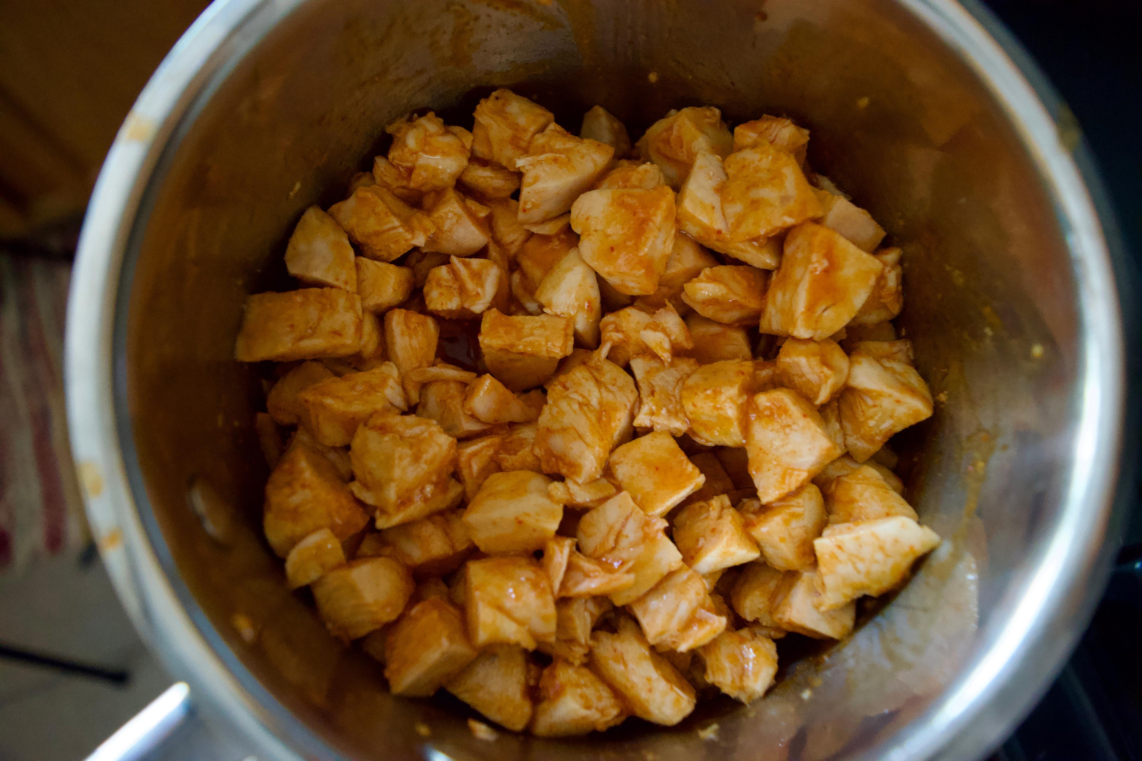 A pan of cubed, cooked chicken coated in hot sauce