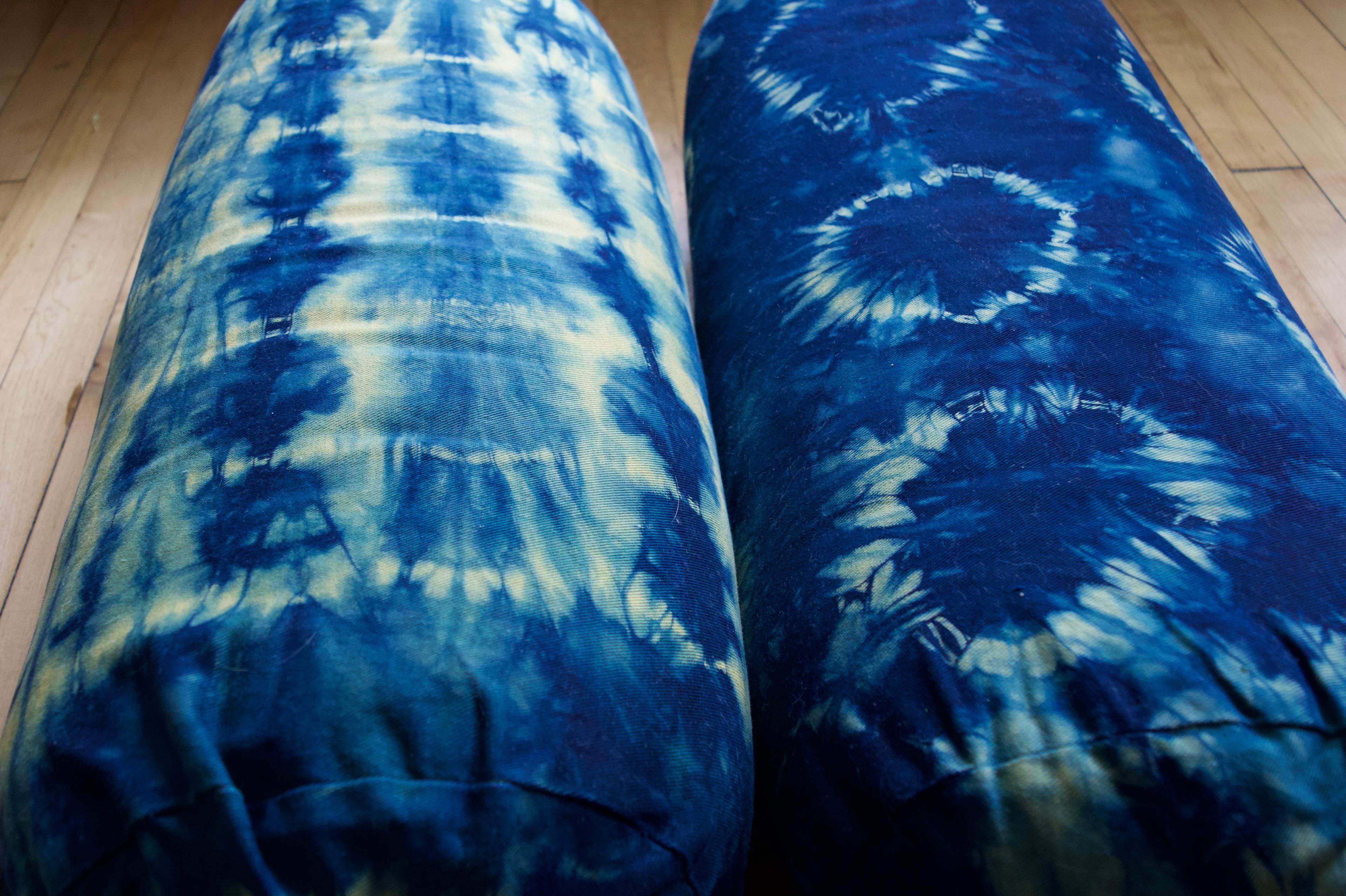 Two yoga bolsters on a wooden floor. One has a grid pattern and the other has a circle pattern. The base is dark blue with yellow patterning.