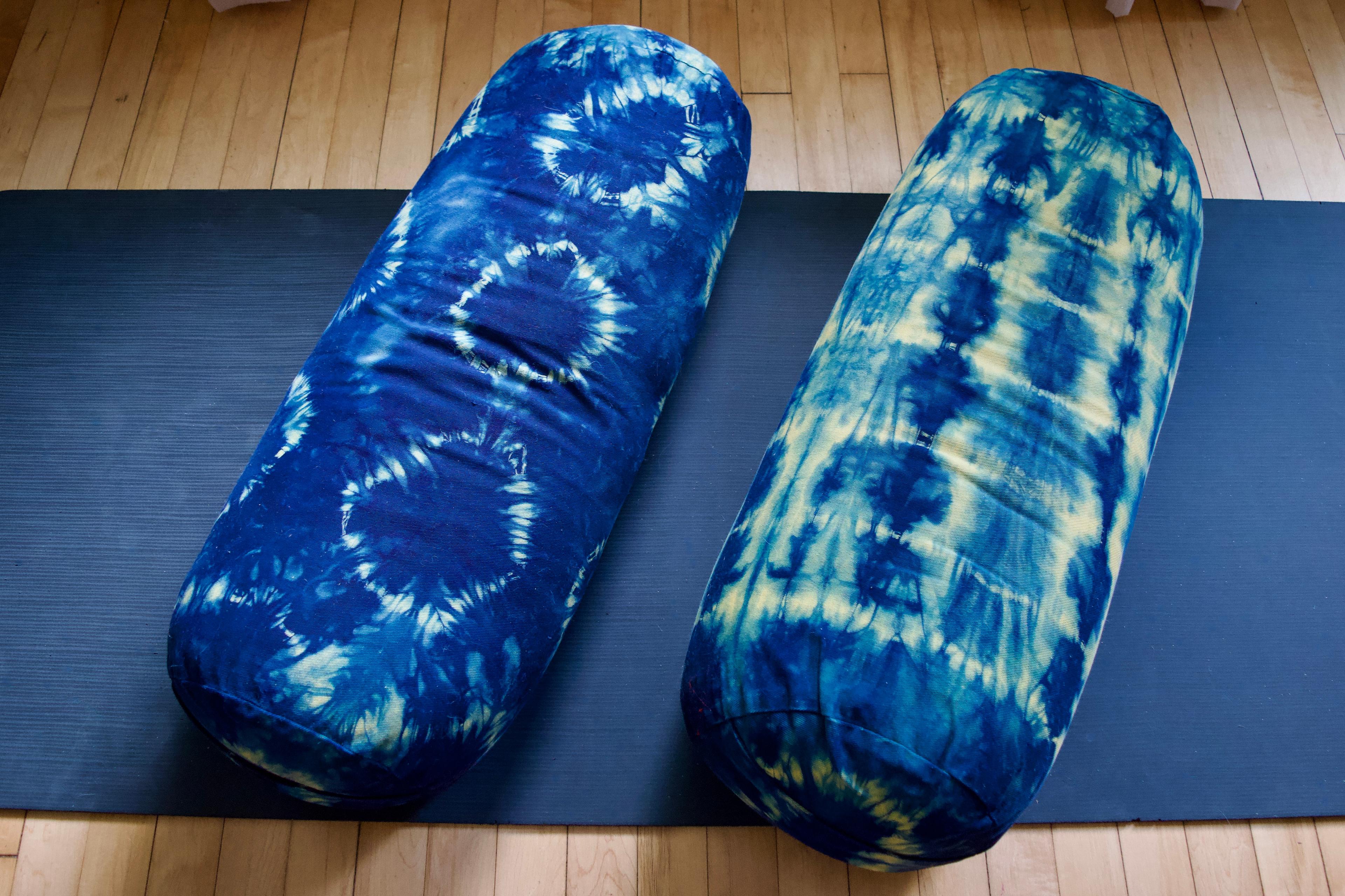 Two blue and yellow yoga bolsters that have been shibori tie dyed resting on a black yoga mat